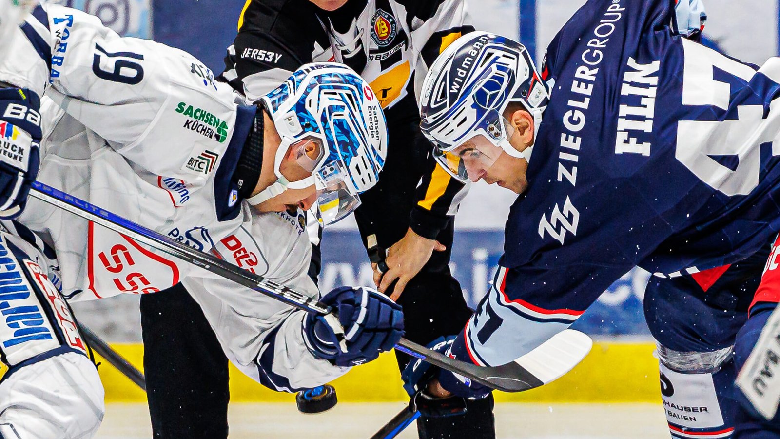 Danke für die Einordnung. Dann passt dieser Alt-Text besser: **Niklas Postel im Trikot der Dresdner Eislöwen beim Bully gegen Vlad Filin von den Blue Devils Weiden.** Etwas ausführlicher: **Niklas Postel, noch im Trikot der Dresdner Eislöwen, beim Bully gegen seinen zukünftigen Teamkollegen Vlad Filin von den Blue Devils Weiden.**
