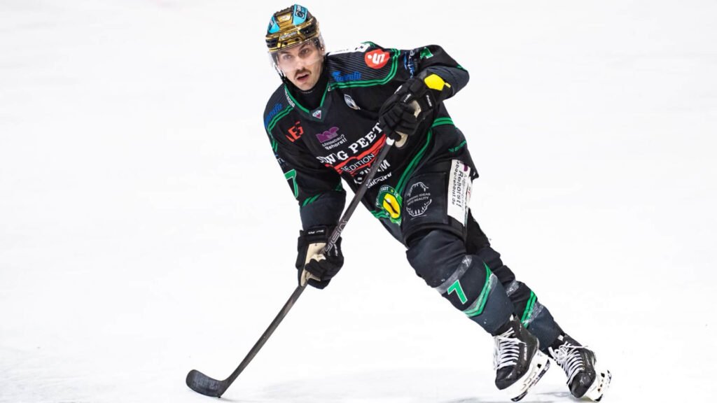Eishockeyspieler Tyler Gron läuft in schwarzer Ausrüstung mit Schläger über das Eis