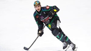 Eishockeyspieler Tyler Gron läuft in schwarzer Ausrüstung mit Schläger über das Eis