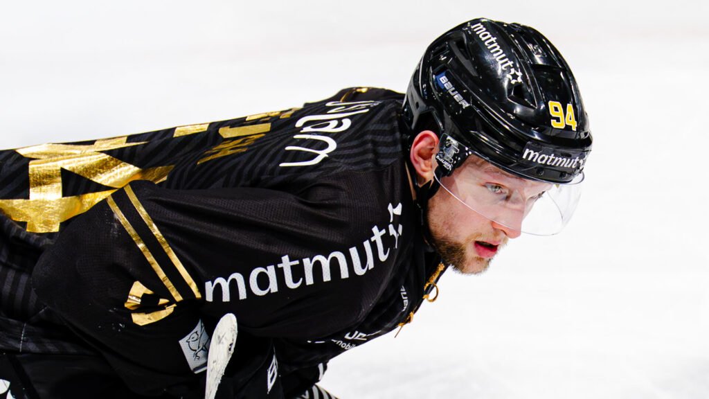 **Alt-Text:** Eishockeyspieler Michael Regush in schwarzem Trikot und schwarzem Helm auf dem Eis, konzentriert nach vorne blickend.