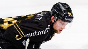 **Alt-Text:** Eishockeyspieler Michael Regush in schwarzem Trikot und schwarzem Helm auf dem Eis, konzentriert nach vorne blickend.
