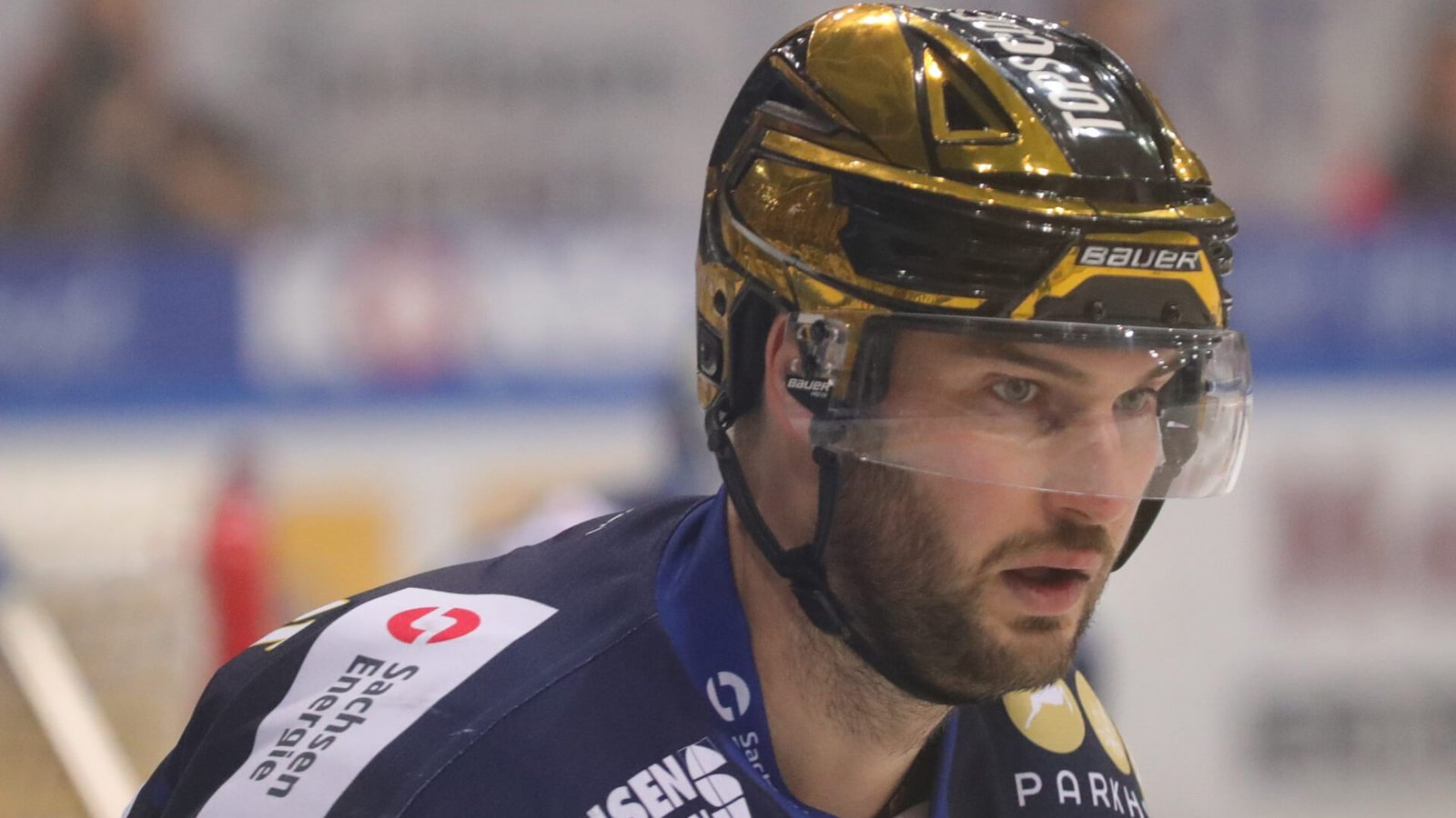 Nahaufnahme von Eishockeyspieler Jordan Knackstedt in blauem Trikot mit Blick nach rechts, der einen glänzenden, goldenen Helm trägt.
